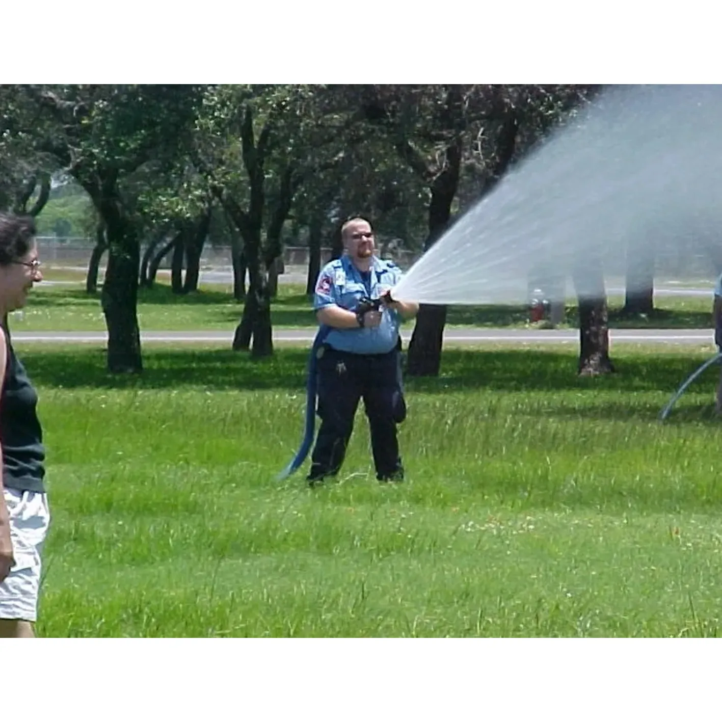 Man using water hose on grassy field.