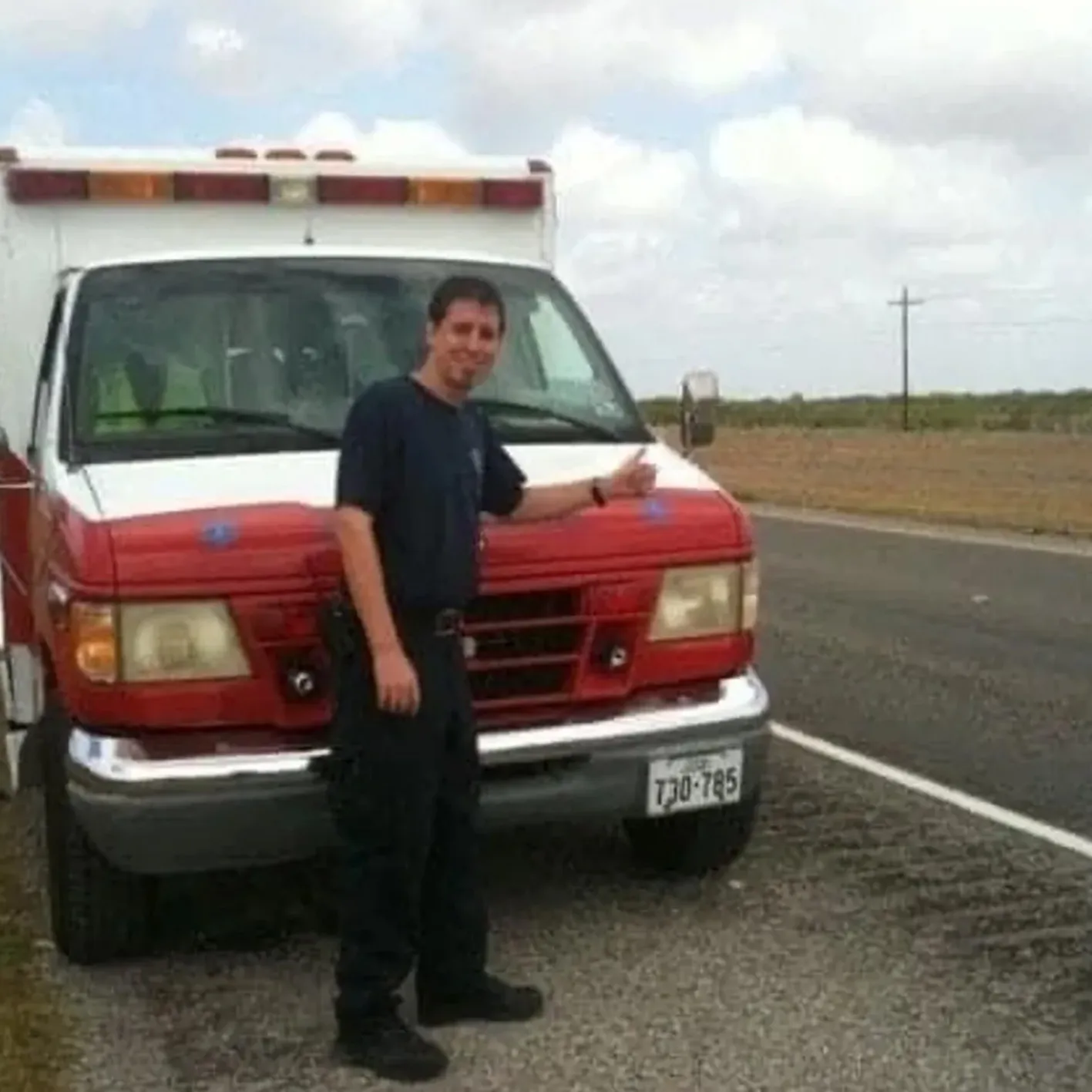 Paramedic posing by ambulance on roadside.