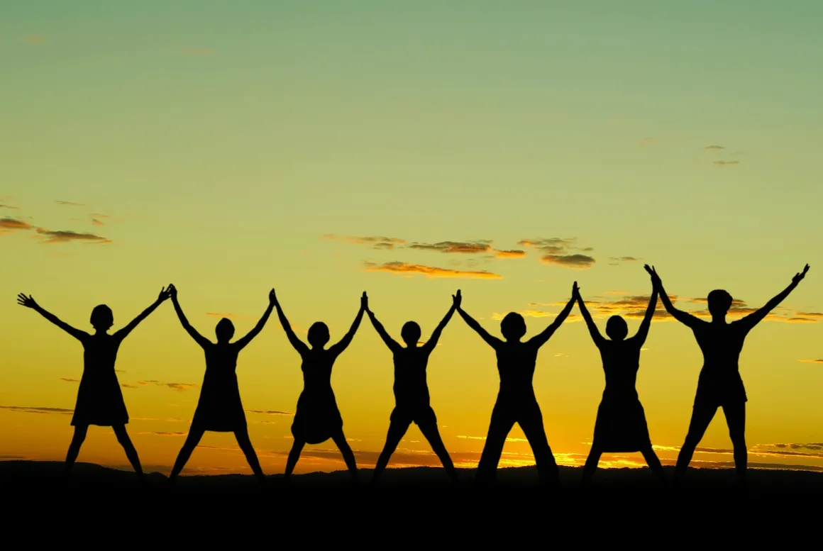 Silhouette of women holding hands at sunset.