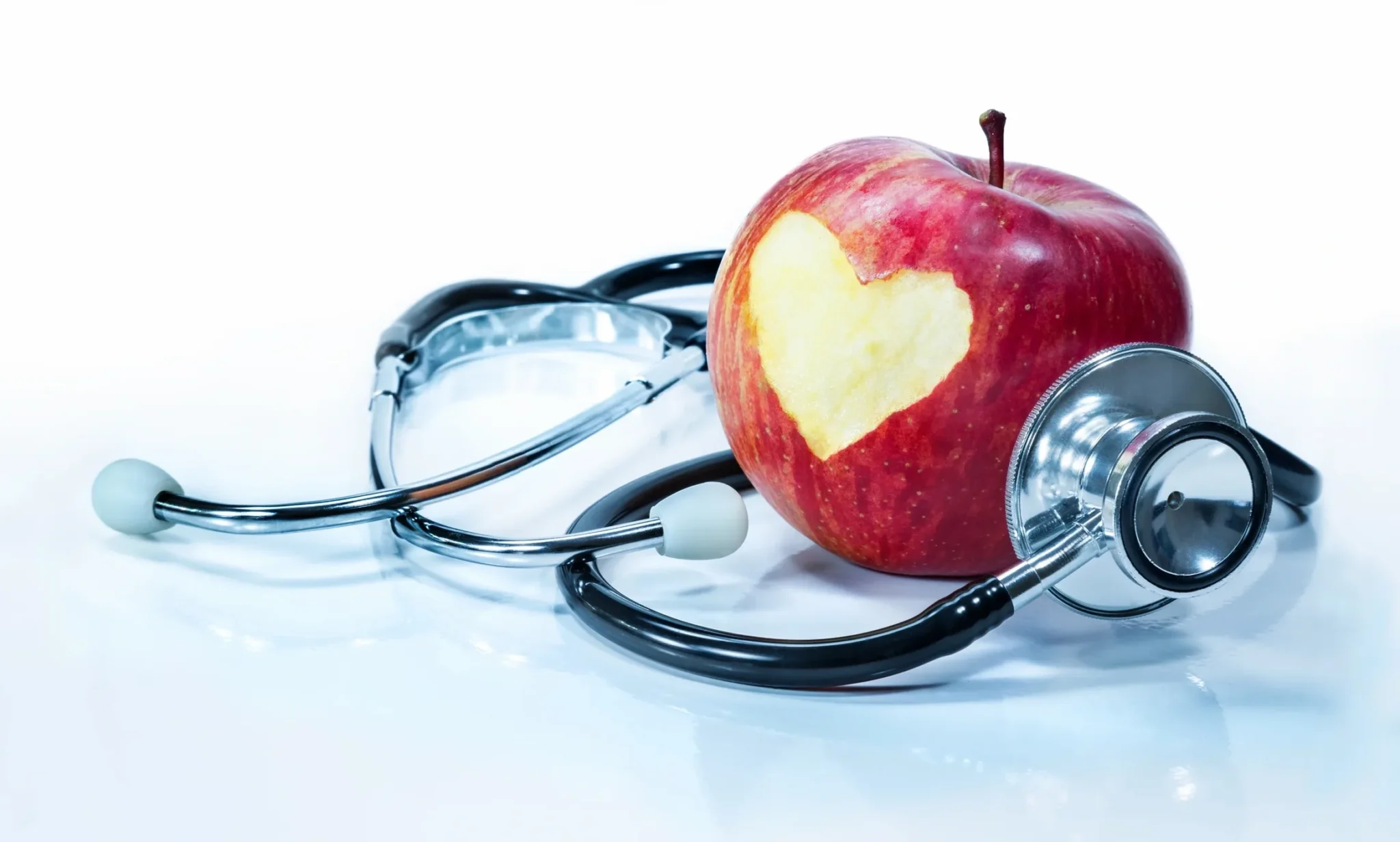 Here's an alt tag for the image: Apple with heart-shaped bite, stethoscope.