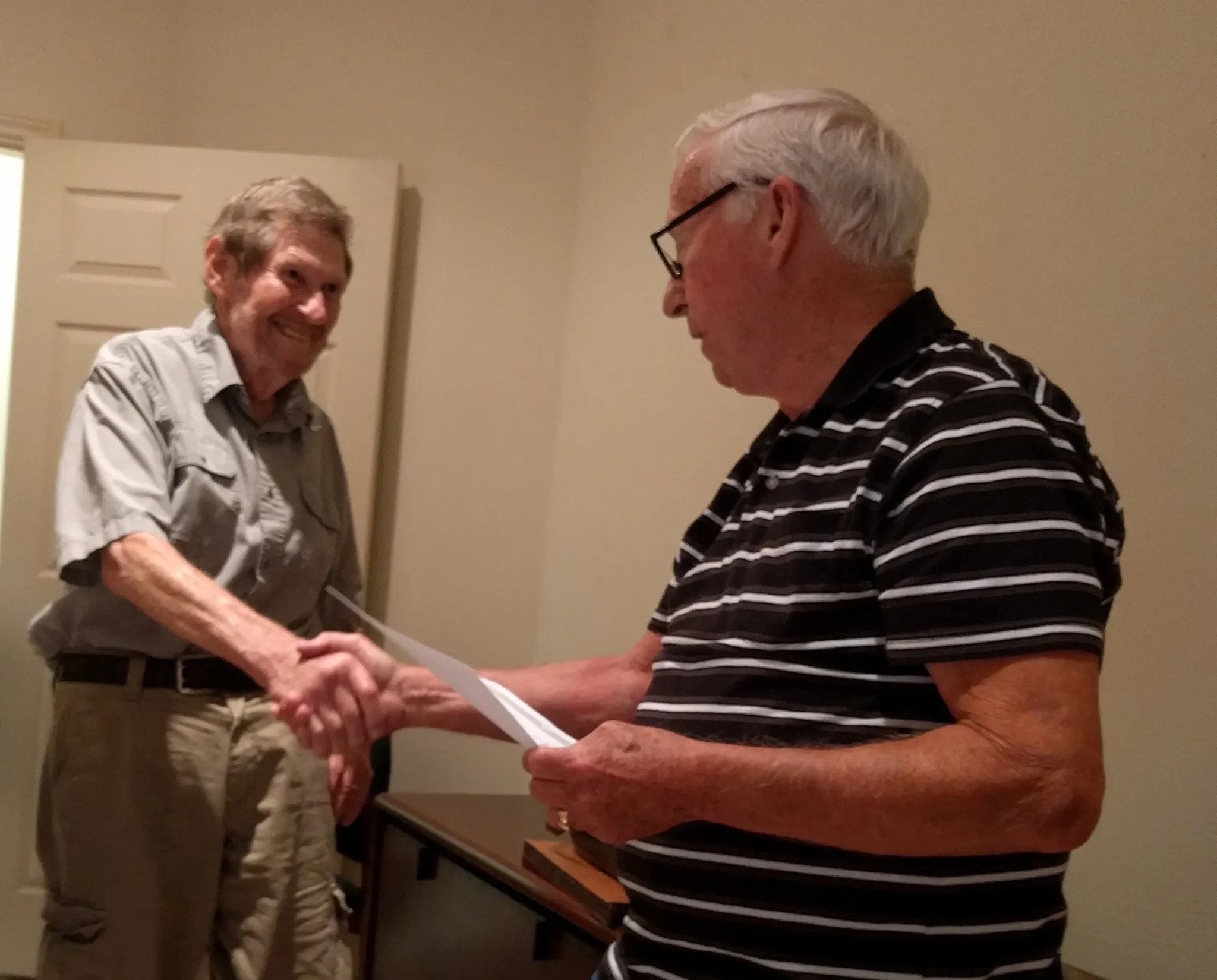 Two men shaking hands, one holding paper.